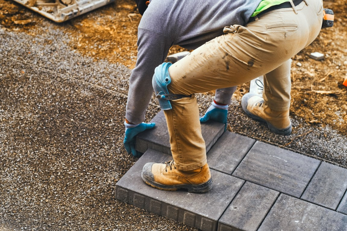 A picture of a man installing paver stones in a paver driveway